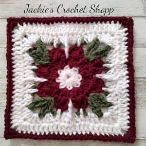 May include: Crocheted square with a red poinsettia flower in the center, surrounded by white and green crochet. The square has a burgundy border.