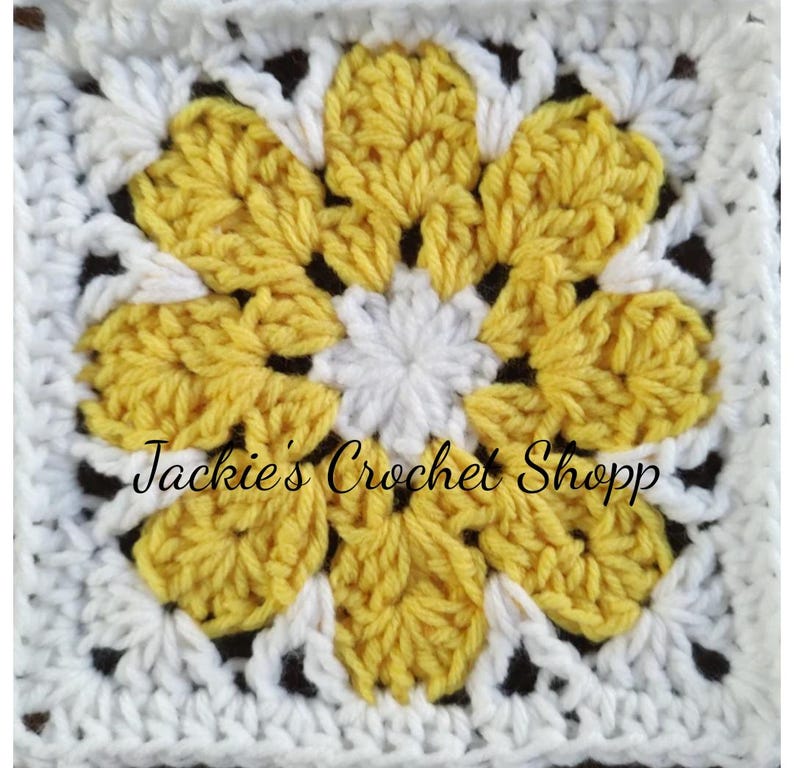 May include: A crochet square with a yellow flower in the center. The flower has six petals and a white center. The square is surrounded by a white border.