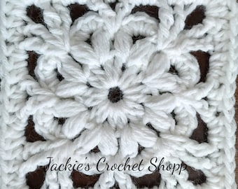Könnte beinhalten: Weißes Häkelquadrat mit einem Blumendesign in der Mitte. Das Quadrat ist mit einer einfachen Häkelmasche gearbeitet und hat einen Rand aus doppelten Häkelmaschen. Der Text "Jackie's Crochet Shop" ist in der Mitte unten im Bild sichtbar.