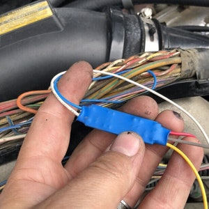 May include: A close-up of a blue electrical connector with red, white, and yellow wires attached. The connector is held in a hand.