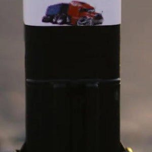 May include: A black cylindrical product with a white label featuring the text "The Ugly Fix®" and an image of a red and blue semi-truck. The product has a rectangular base and is likely related to automotive repair.