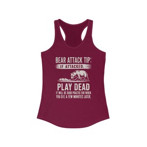 May include: A burgundy racerback tank top with white text that reads "BEAR ATTACK TIP: IF ATTACKED, PLAY DEAD." A graphic of a bear and a small animal is below the text. The bottom text reads "IT WILL BE GOOD PRACTIC FOR WHEN YOU DIE A FEW MINUTES LATER."