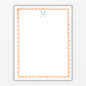 May include: A rectangular sheet of white stationery featuring a scalloped border in a soft peach color. Centered at the top of the page is the capital letter M printed in a light blue serif font, providing a clear and simple design for correspondence.