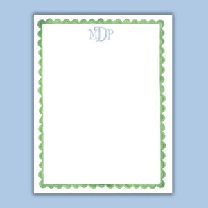 May include: White stationery with a green scalloped border and a light blue monogram. The paper has a simple, elegant design, perfect for personalized notes or letters. The background is a light blue.