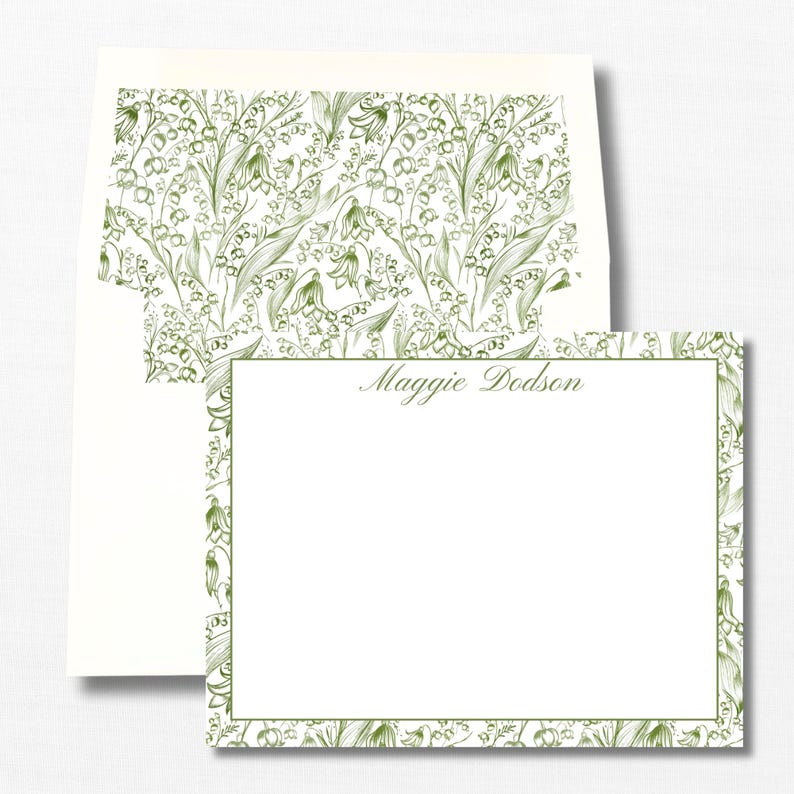 May include: A white card with a green border featuring a floral pattern of lily of the valley. The card has the name "Maggie Dodson" printed in cursive at the top.