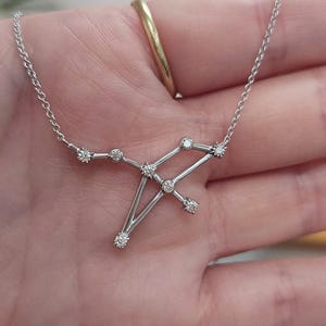 May include: A silver necklace with a constellation pendant featuring small diamonds. The pendant is shaped like the constellation Sagittarius.