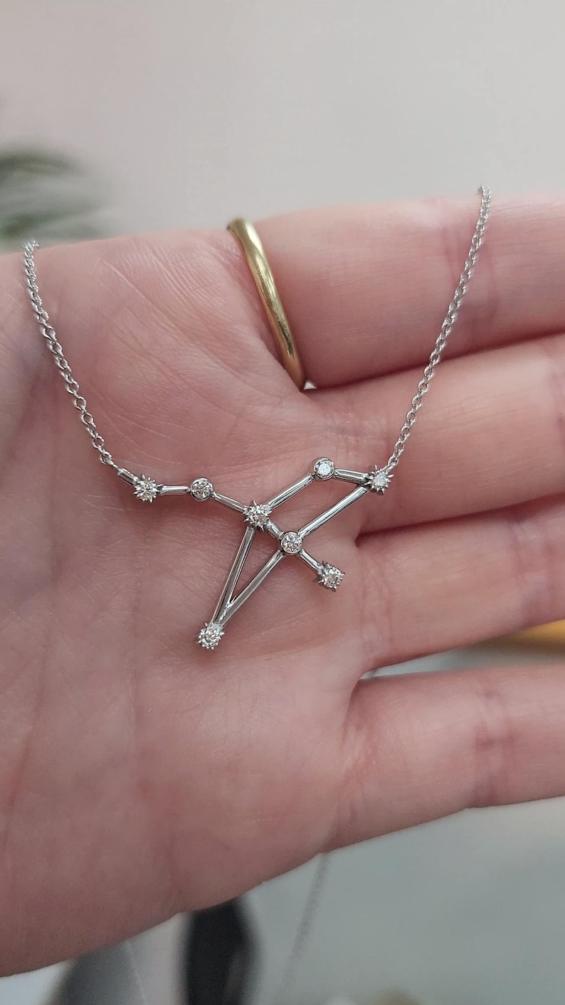 May include: A silver necklace with a constellation pendant featuring small diamonds. The pendant is shaped like the constellation Sagittarius.