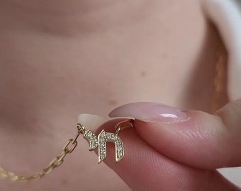 May include: A gold chain necklace with a pendant featuring the Hebrew letter 'Chai' set with small diamonds.