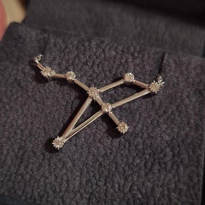 May include: A silver necklace with a constellation pendant featuring small, clear diamonds. The pendant is shaped like a constellation of stars.