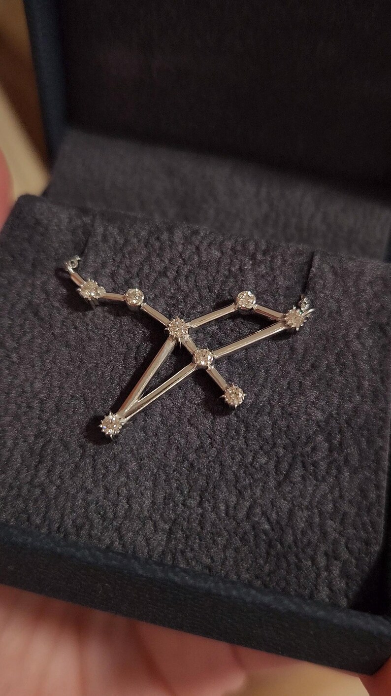 May include: A silver necklace with a constellation pendant featuring small, clear diamonds. The pendant is shaped like a constellation of stars.