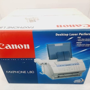 May include: Canon FAXPHONE L80 laser fax printer in its original box. The box is white with red and blue accents, and features the Canon logo and product information. The printer is gray and white.