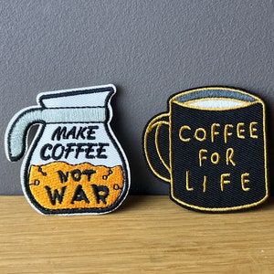 Könnte beinhalten: Zwei gestickte Bügelbilder. Eines ist eine weiße Kaffeekanne mit orangefarbenem Kaffee und dem Text "Make Coffee Not War". Das andere ist eine schwarze Kaffeetasse mit dem Text "Coffee For Life".