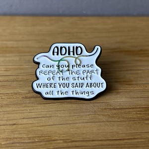 Könnte beinhalten: Weißer Emaille-Pin mit schwarzem Rand. Der Pin zeigt das Wort "ADHS" über dem Satz "Können Sie bitte den Teil des Stoffs wiederholen, wo Sie über all die Dinge gesprochen haben."