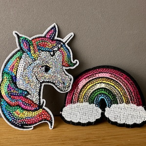 Könnte beinhalten: Zwei bunte Bügelbilder, eines mit einem Regenbogen mit Wolken und das andere mit einem Einhornkopf. Beide Patches sind mit schillernden Pailletten bedeckt.