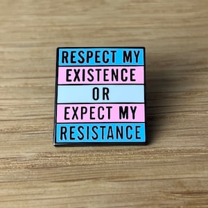 Könnte beinhalten: Eine blaue, rosa und weiße Emaille-Anstecknadel mit dem Text "Respect My Existence Or Expect My Resistance".