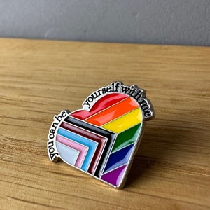 Könnte beinhalten: Eine silberne herzförmige Anstecknadel mit einem Regenbogenmuster und dem Text "you can be yourself with me".