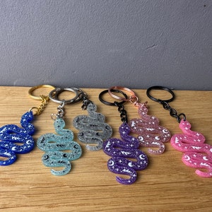 Könnte beinhalten: Eine Sammlung von schlangenförmigen Schlüsselanhängern mit Glitzer in verschiedenen Farben: Blau, Hellblau, Silber, Lila und Rosa. Jeder Schlüsselanhänger hat ein Himmelsdesign mit Sternen und Monden. Die Schlüsselanhänger haben unterschiedlich farbige Ringe und Ketten.