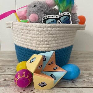 May include: A blue and white woven basket filled with Easter eggs, a grey plush toy wearing sunglasses that say "Man looks at the outside, but the looks at the", and a colourful paper fortune teller.