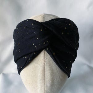May include: Black turban-style headband with gold metallic flecks. The fabric is twisted at the front, creating a stylish accessory. This headband is designed to be worn around the head.