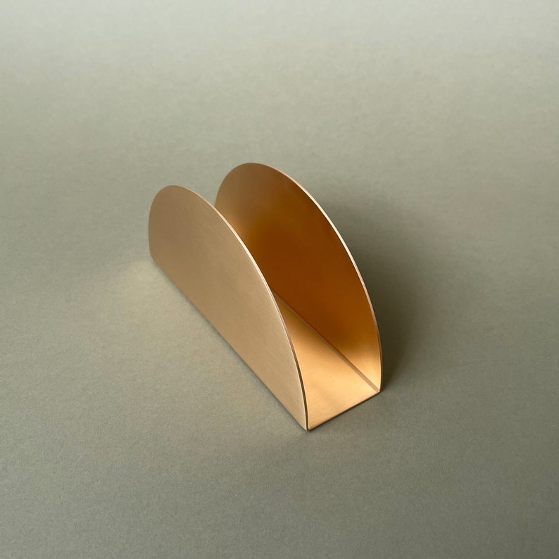 Pu&ograve; includere: Un porta tovaglioli in metallo dorato con un design curvo. Il porta tovaglioli &egrave; composto da due forme a semicerchio che sono unite.