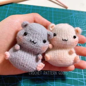 Puede incluir: Dos peluches de hámster tejidos a crochet, uno gris y otro crema, con ojos negros y mejillas rosadas. Los peluches están sentados en una mano, con el texto "CROCHET PATTERN GOODS" visible debajo.