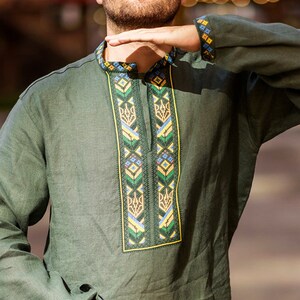 K&ouml;nnte beinhalten: Ein Mann tr&auml;gt ein gr&uuml;nes Leinenhemd mit Stickereien. Die Stickerei zeigt ein traditionelles ukrainisches Muster in Gelb, Blau und Gr&uuml;n.