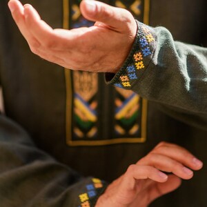 K&ouml;nnte beinhalten: Ein gr&uuml;nes Langarmhemd mit Stickereien in Gelb, Blau und Orange. Die Stickerei befindet sich an den Manschetten und auf der Vorderseite des Hemdes.