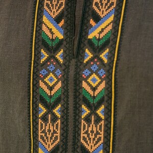 K&ouml;nnte beinhalten: Ein braunes Leinenhemd mit einem schwarzen, gelben, blauen, gr&uuml;nen und orangefarbenen Stickmuster. Das Muster zeigt ein traditionelles ukrainisches Muster.