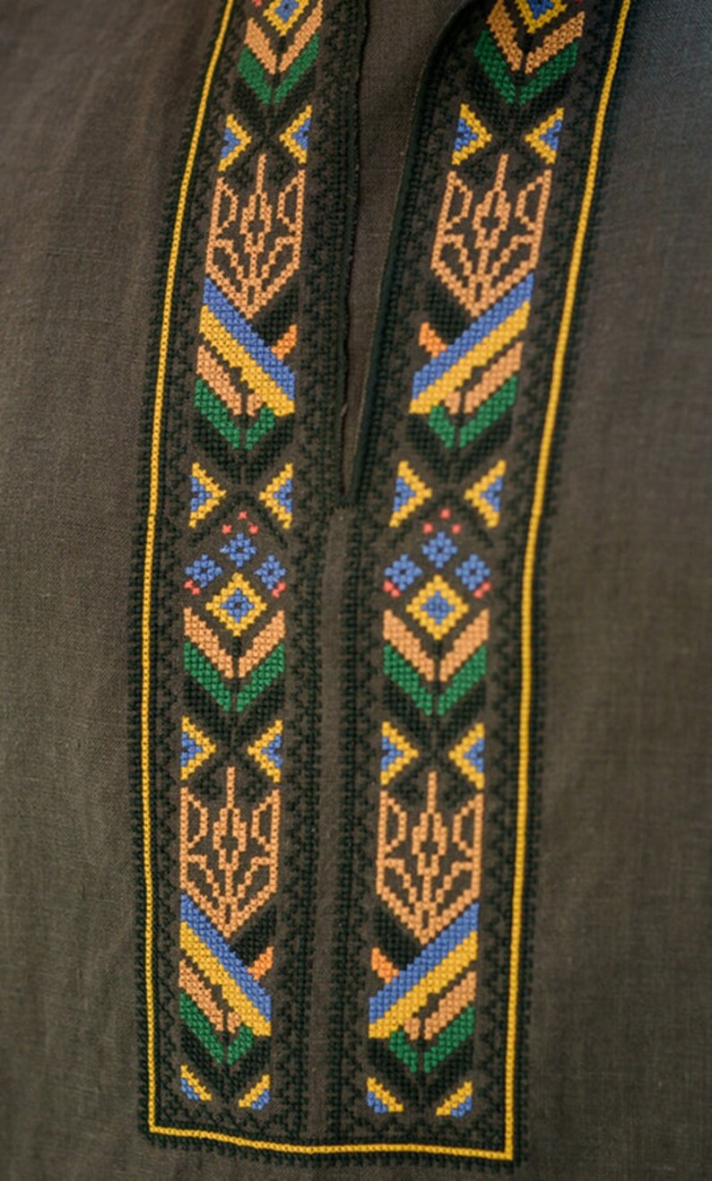 K&ouml;nnte beinhalten: Ein braunes Leinenhemd mit einem schwarzen, gelben, blauen, gr&uuml;nen und orangefarbenen Stickmuster. Das Muster zeigt ein traditionelles ukrainisches Muster.