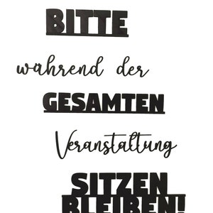May include: Black and white sign with the text "Bitte w&auml;hrend der gesamten Veranstaltung sitzen bleiben!" which translates to "Please remain seated throughout the entire event!"