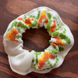 May include: A white scrunchie with a green, orange, and yellow geometric pattern.