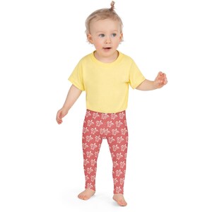 May include: A toddler wearing a yellow short-sleeved shirt and red leggings with a white turtle pattern.