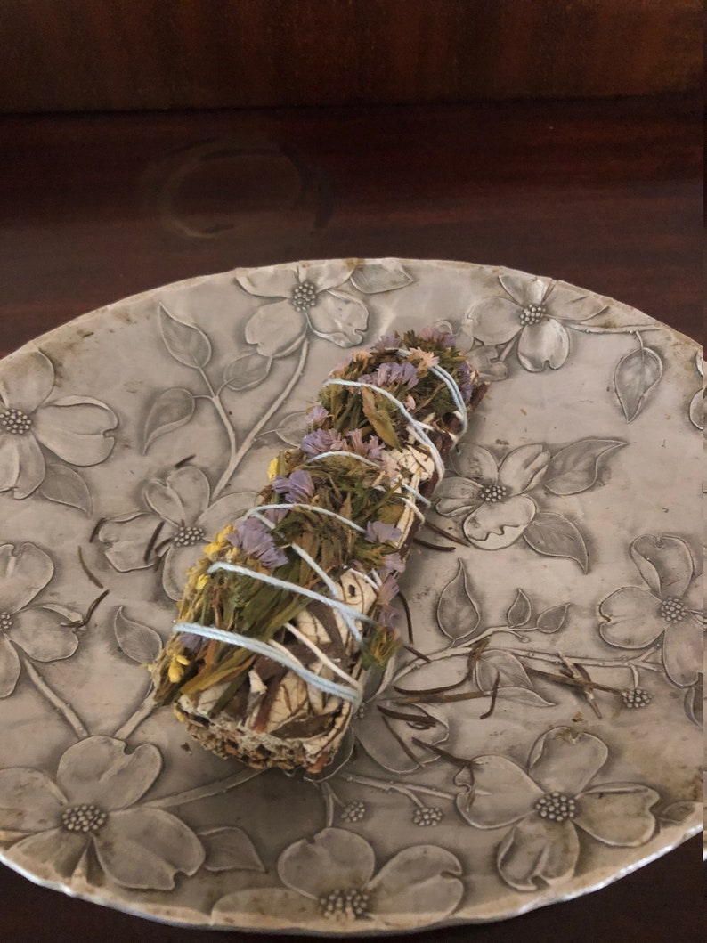 Peut inclure: Un b&acirc;tonnet de sauge avec des herbes et des fleurs s&eacute;ch&eacute;es, li&eacute; avec de la ficelle, sur une assiette florale grise.