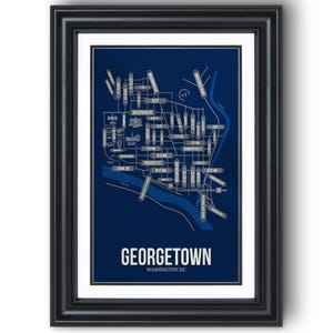 May include: A framed print featuring a detailed map of Georgetown, Washington DC, in white and light blue on a dark blue background. The print includes street names and a river, with the word "GEORGETOWN" prominently displayed.