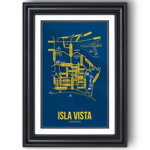 May include: Framed Isla Vista, California map art print. The print features a detailed yellow street map on a dark blue background. The text "ISLA VISTA CALIFORNIA" is displayed at the bottom. The print is encased in a black frame.
