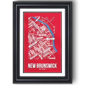 May include: Framed map print of New Brunswick, New Jersey, in a black frame. The map features white street names and a blue river against a red background. The city name is displayed in large white letters at the bottom.