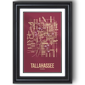 May include: Framed map print of Tallahassee, Florida. The map features a gold-colored street grid and landmarks against a burgundy background. The city name is displayed in gold at the bottom, encased in a black frame.