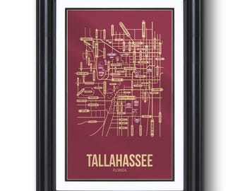 May include: Framed map print of Tallahassee, Florida. The map features a gold-colored street grid and landmarks against a burgundy background. The city name is displayed in gold at the bottom, encased in a black frame.