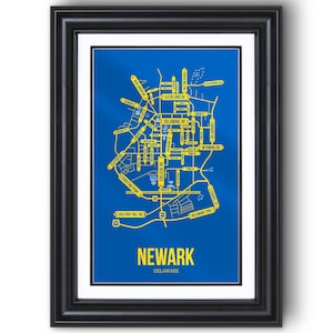May include: Framed map print of Newark, Delaware, featuring a blue background with yellow street names and roads. The city name is displayed in bold yellow letters at the bottom, with the state below. The print is encased in a black frame.