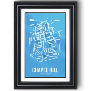 May include: Framed map print of Chapel Hill, North Carolina, featuring a detailed white street layout against a light blue background. The town's name is displayed in white block letters at the bottom, encased in a black frame.