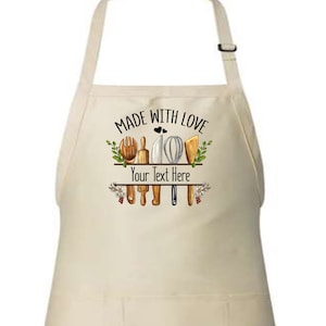 May include: A white cotton apron with a pocket, featuring a design of kitchen utensils and the text "Made with Love" and "Your Text Here".