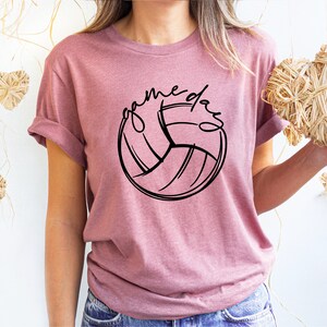 K&ouml;nnte beinhalten: Ein pinkfarbenes T-Shirt mit einer schwarzen Volleyballgrafik und dem Text "game day" um den Ball herum.