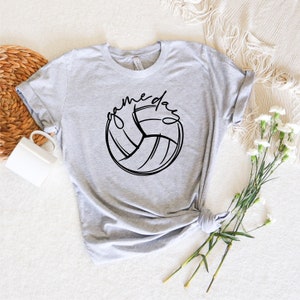 K&ouml;nnte beinhalten: Ein graues T-Shirt mit einer schwarzen Volleyballgrafik und dem Text "game day" in einer Schriftart.