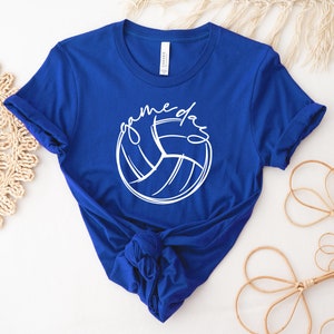 K&ouml;nnte beinhalten: Ein k&ouml;nigsblaues T-Shirt mit einer wei&szlig;en Volleyballgrafik und dem Text "game day" in wei&szlig;er kursivschrift.
