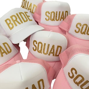 May include: A set of pink and white trucker hats with gold glitter lettering. The hats say "Bride" and "Squad".