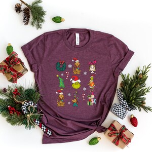 Może przedstawiać: Bordowy t-shirt z grafiką świąteczną przedstawiającą Grincha, Cindy Lou Who i inne postacie z filmu "Grinch: świąt nie będzie!"