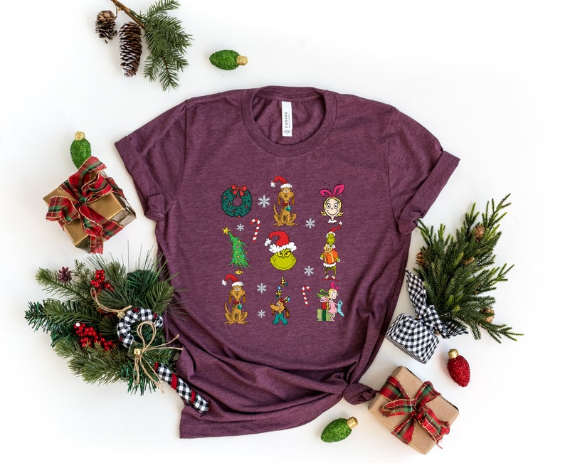 Może przedstawiać: Bordowy t-shirt z grafiką świąteczną przedstawiającą Grincha, Cindy Lou Who i inne postacie z filmu "Grinch: świąt nie będzie!"