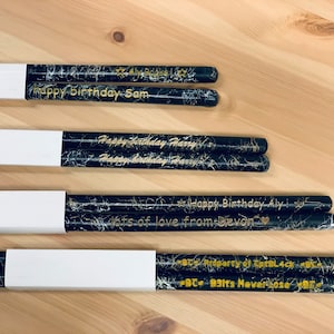 May include: Four pairs of black and gold drumsticks with personalized messages. The messages include "Happy Birthday Sam", "Happy Birthday Harry", "Happy Birthday Aly lots of love from Devon", and "BC B3Its Never Lose".