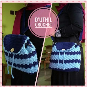 May include: A blue and light blue crocheted bag with a drawstring closure and a flap. The bag has a shoulder strap and is worn by a person. The bag has the text "D'UTHIL CROCHET" on it.