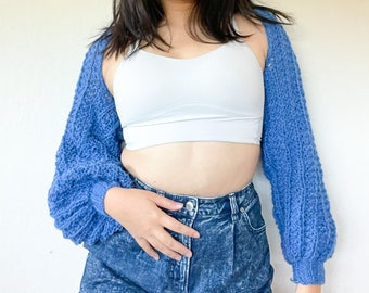 May include: A blue knitted cardigan with long sleeves and a loose fit. The cardigan is open in the front and has a textured knit pattern.